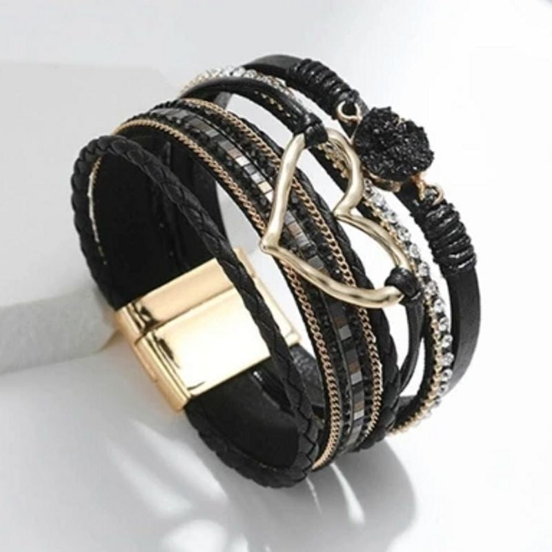 Bracelet amour de cœur, wrap bohème multilanière en cuir PU présenté sur le poignet d'une femme élégante vêtu de noir avec breloques en pierre de résine et cœur ajouré doré, rivière de strass en cristal et fines chaînes en alliage de zinc. Présenté dresser sur son fermoir magnétique doré - Coloris noir.