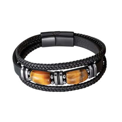 Vue frontale du bracelet Apex révélant sa structure multi-rangs en cuir noir aux textures contrastées, où deux gemmes d’œil de tigre aux reflets fauves jaunes brun sont encadrées par des bagues en acier sur un fond épuré.