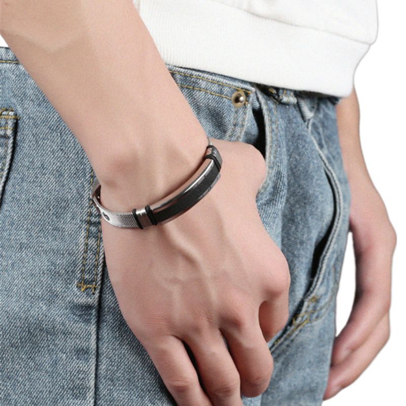Bracelet ardillon à maille milanaise en acier argenté sur le poignet d'un homme vêtu d'un pantalon en jean bleu - coloris barrette noire