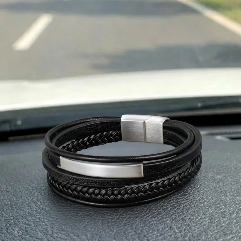 Vue en situation. Le bracelet Axis cuir souple noir posé à plat, sa géométrie et son tube rectangulaire brillent sous la lumière, face à l'horizon de la route.