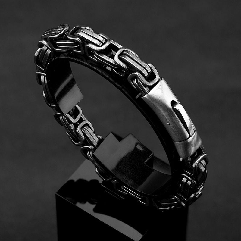 Vue sur le robuste bracelet biker avec sa chaine complexe de couleur argent vieilli -Maillons 7 mm - présentation sur un socle cubique noir posé sur plateau en bois noir