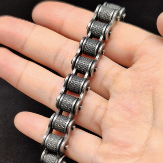 Bracelet biker avec maillons moletés et fermoir en acier inoxydable présenté autour des doigts d'une main d'homme - coloris argent vieilli