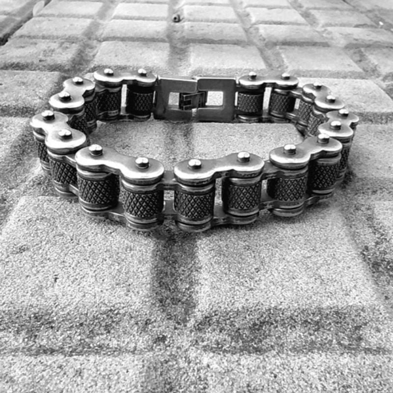 Bracelet biker avec maillons moletés et fermoir crochet à clip en acier inoxydable posé sur un sol carrelé gris- coloris de l'acier argent vieilli
