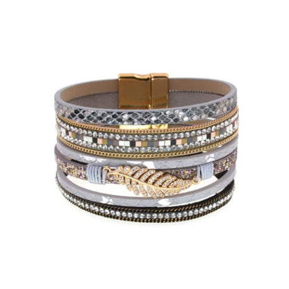 Bracelet bohème chic, wrap multilanière en cuir PU avec breloque feuille de fougère dorée et ornée de strass blanc en cristal, son fermoir magnétique est de couleur or. Coloris gris.