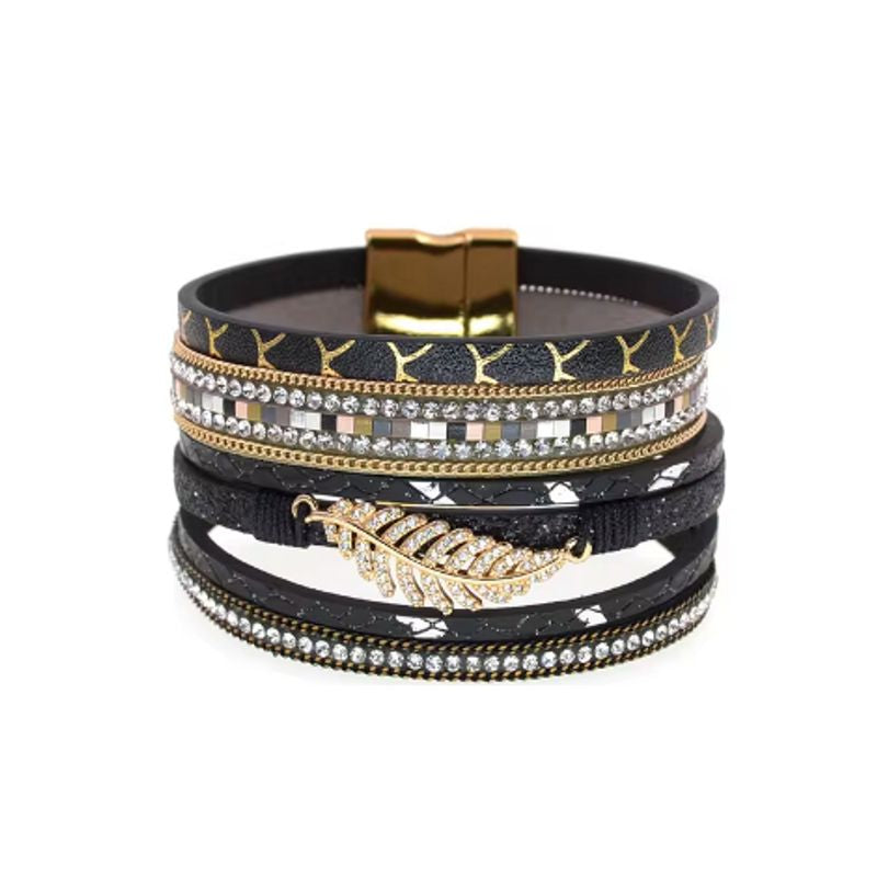 Bracelet bohème chic, wrap multilanière en cuir PU avec breloque feuille de fougère dorée et ornée de strass blanc en cristal, son fermoir magnétique est de couleur or. Coloris noir.