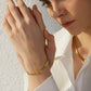 Bracelet chaîne à maillions plats cubains en acier inoxydable présenté sur un poignet de jeune et jolie femme vêtu d'une chemise blanche aux manches longues - zircone cubique - coloris or, plaqué 18 K