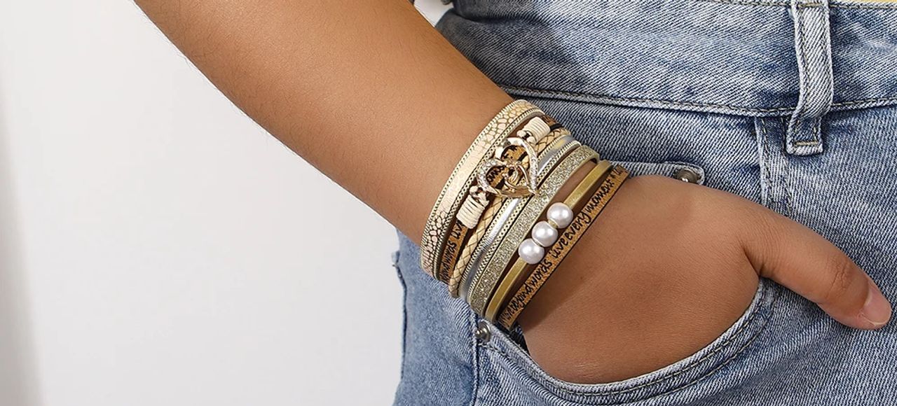 Bracelet cœur bohème doré avec perles, wrap bohème mantras pour femme en cuir PU de couleur beige présentée autour d'un poignet féminin à la main enfouie dans la poche de son jean bleu délavé.