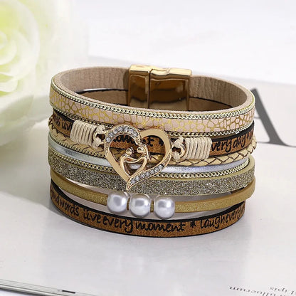 Bracelet cœur mère et enfant dorés multi-rangs, cuir beige microfibre végan imprimé, perles blanches, posé sur fond floral.