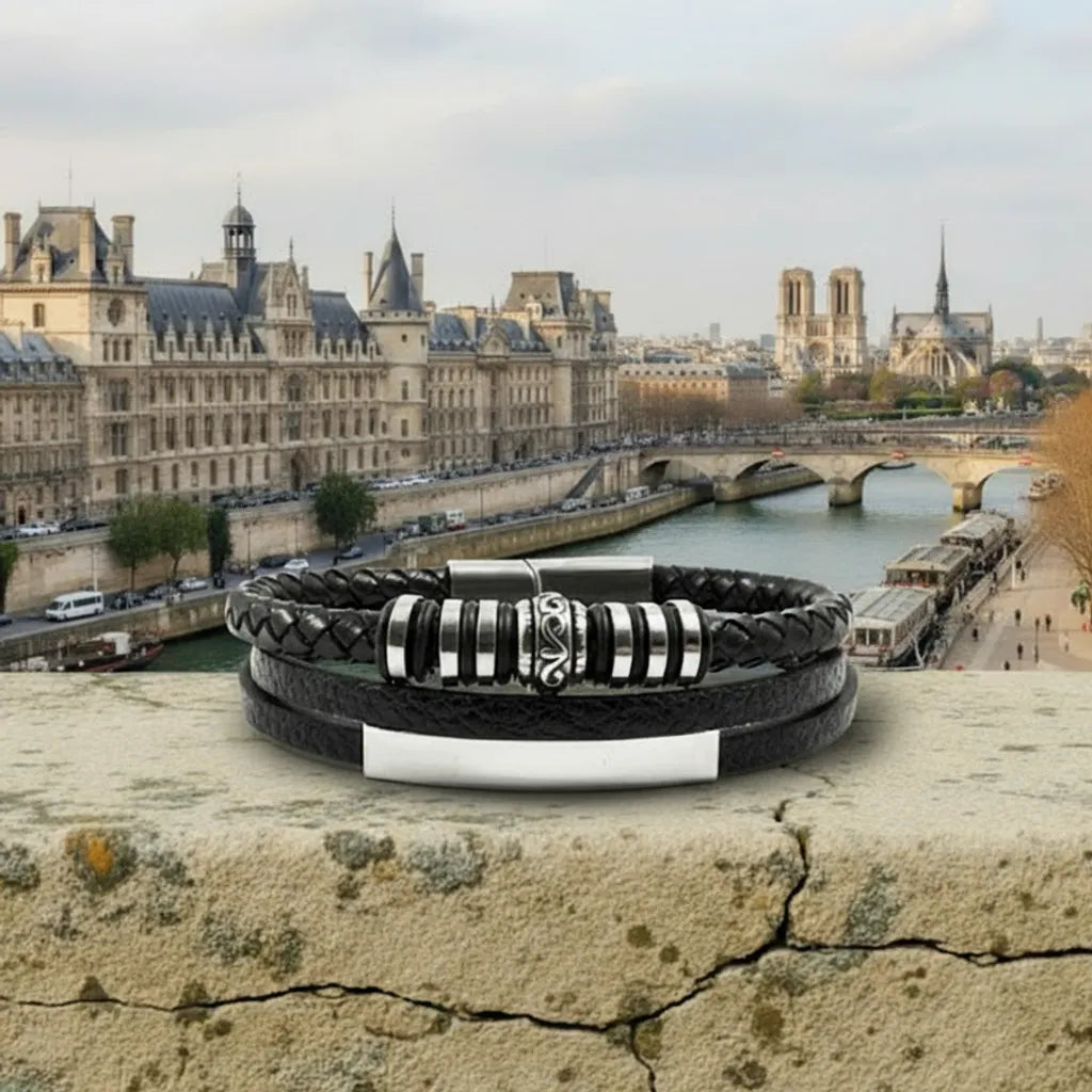 Vue de face sur les quais. Le bracelet Corax multi-rangs cuir noir posé à plat sur la rambarde. La frise gothique et les bagues capturent l'esprit de la Seine.