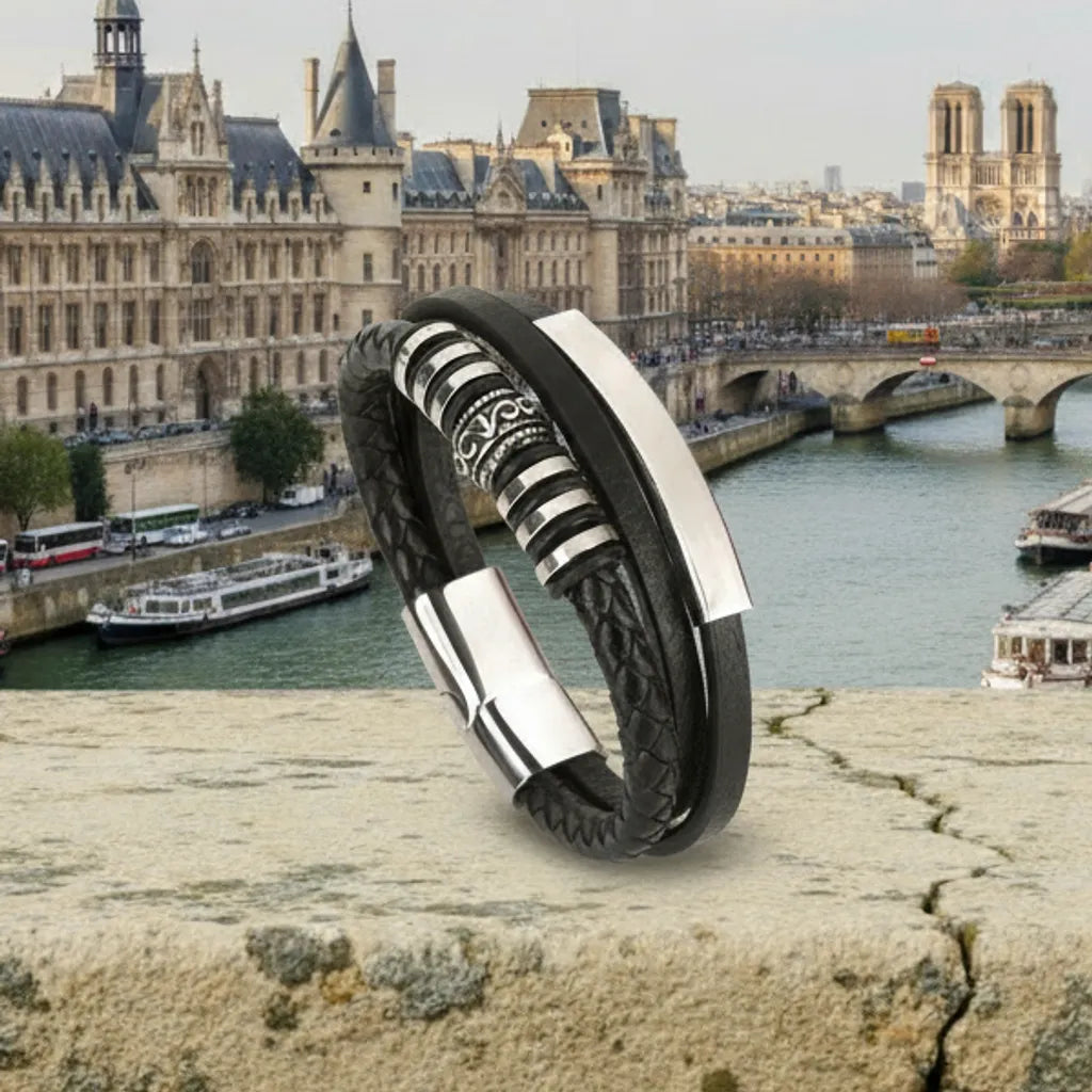 Contexte historique. Le bracelet Corax multi-rangs en équilibre, ses lanières mettant en lumière la frise gothique et l'acier inoxydable, face à l'architecture parisienne.