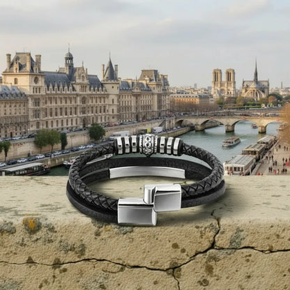 Détail authentique. Le bracelet Corax multi-rangs cuir noir, fermoir entrouvert, reposant sur la pierre. La frise gothique et l'élégance du cuir face à la Seine.