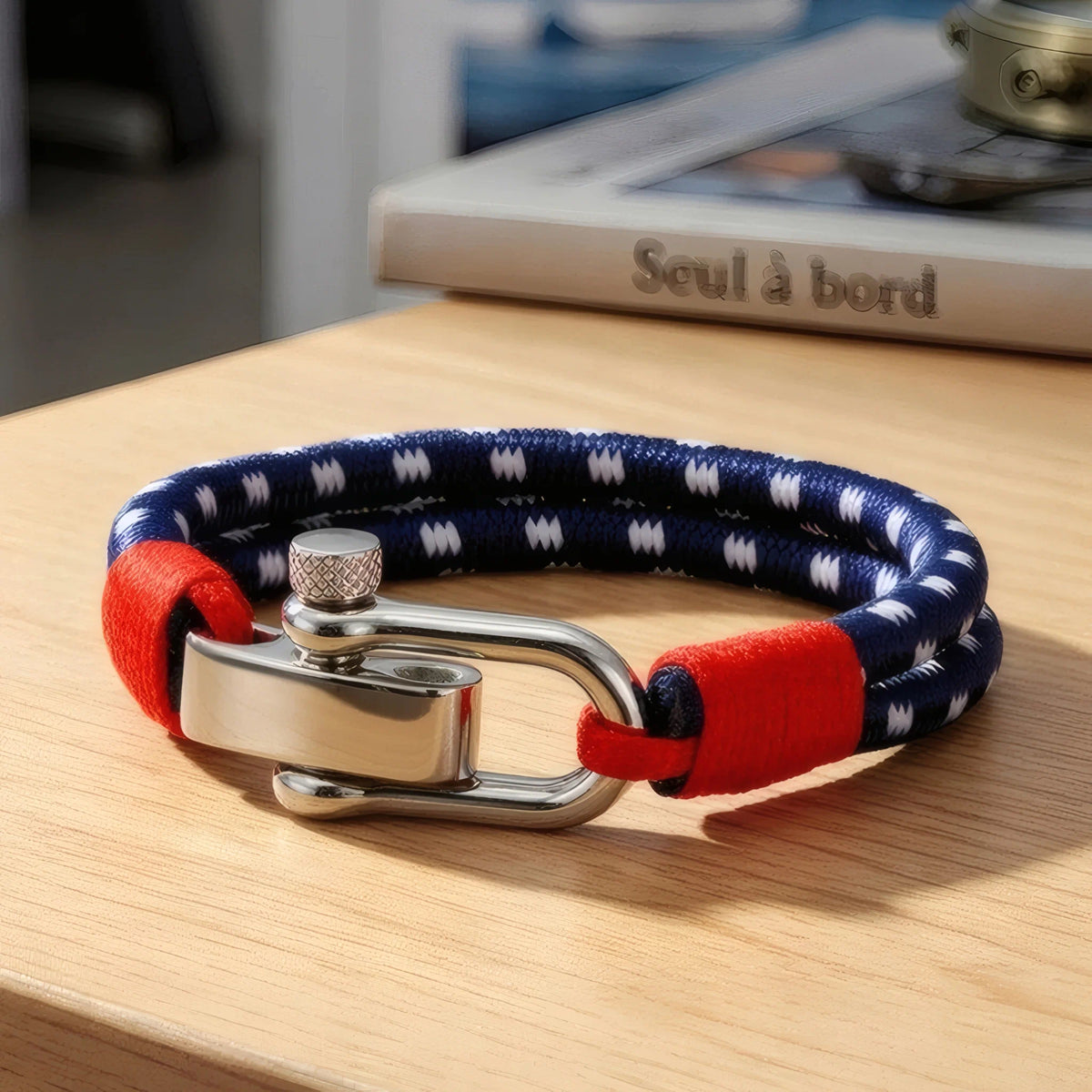 Bracelet marin Nautis posé sur table bois à côté bouquin ambiance nautique épurée.
