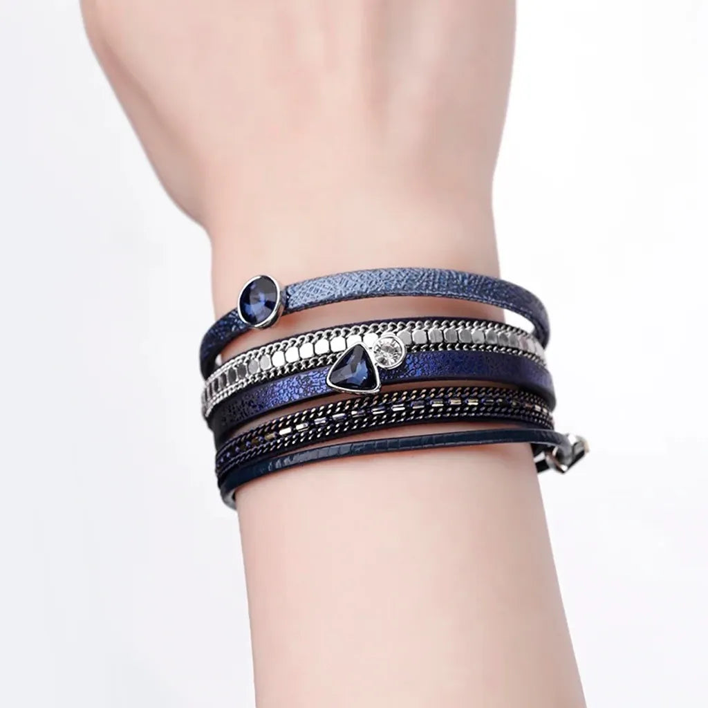 Bracelet Cristal de lumière bleu marine sur un avant-bras nu. Les charms géométriques captent la lumière sur la peau.