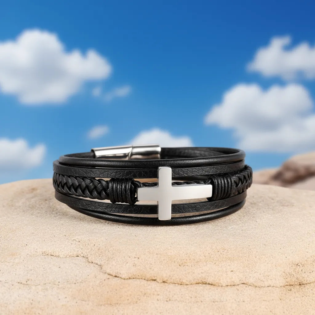 Vue de face du bracelet en cuir multi-rangs, posé à plat sur un rocher avec croix latine sur fond de ciel bleu.