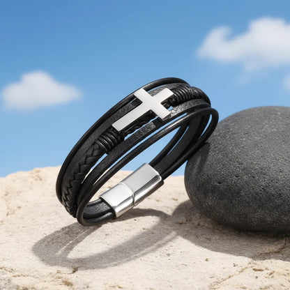 Bracelet multi-rangs incliné sur une pierre. La vue de profil du cuir et de la croix latine est sublimée par un ciel bleu.