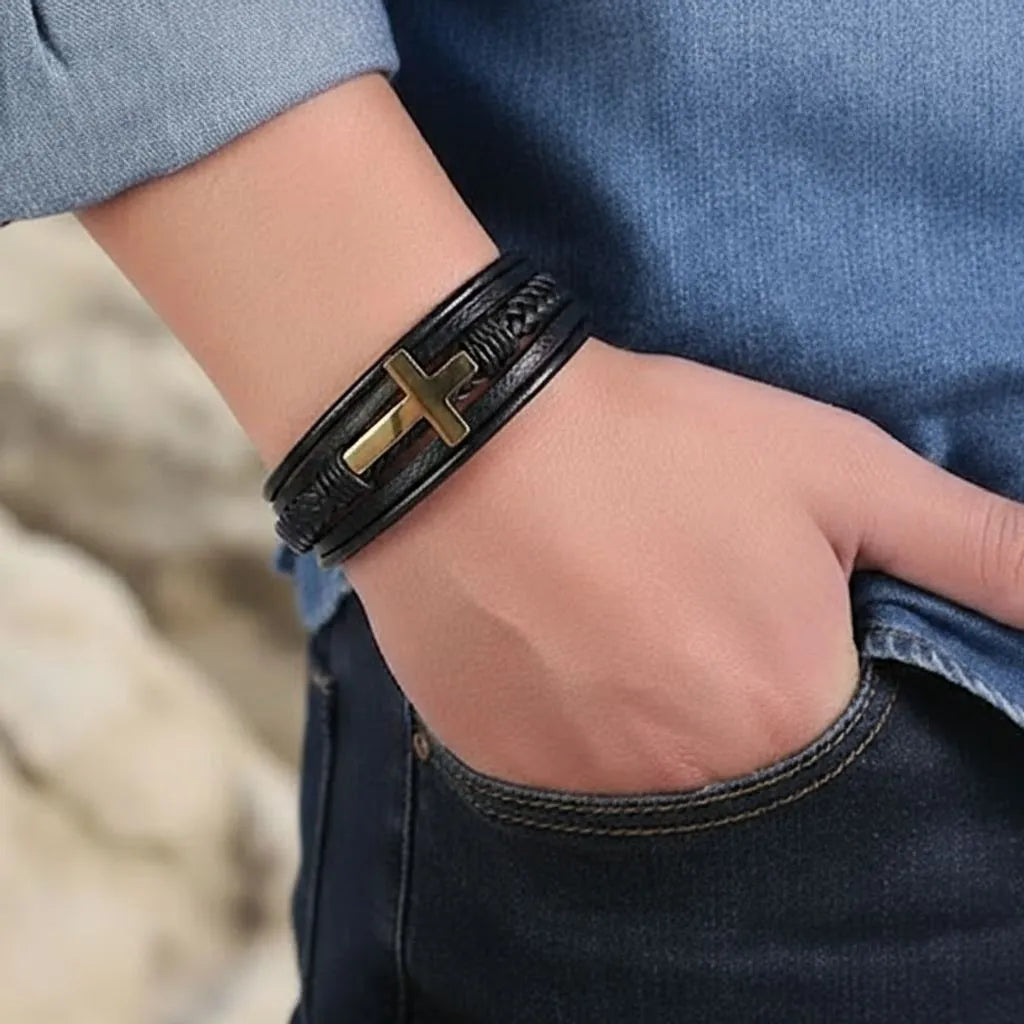 Gros plan du bracelet Croix Latine en cuir noir porté au poignet d'un homme en jean, main dans la poche, vu de profil.