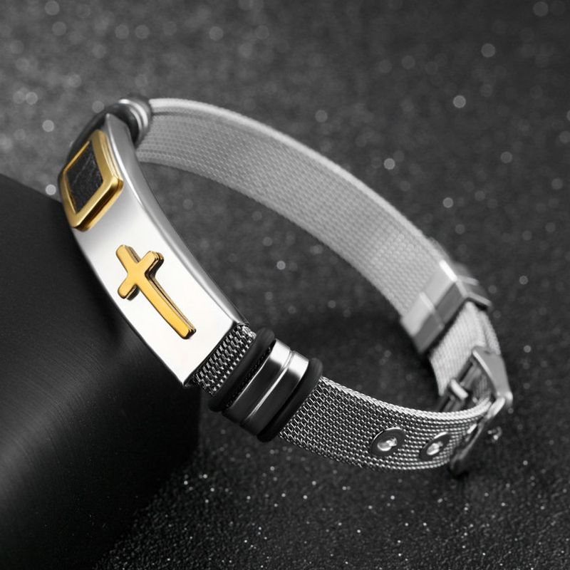 Bracelet boucle ardillon avec croix latine posé sur l'angle d'une boite en cuir noir - sangle à maille milanaise en acier inoxydable - coloris argent et or