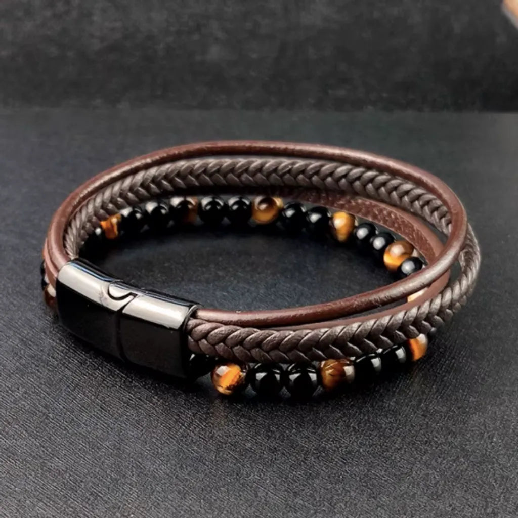 Bracelet en cuir tressé marron avec perles onyx noir et œil de tigre jaune, présenté à plat avec une vue à gauche sur son fermoir magnétique noir élégant. Le fond noir intensifie les textures et la sophistication du design.