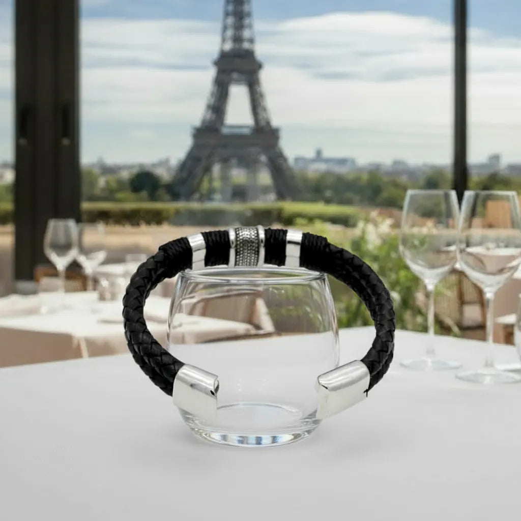 Le bracelet Cylindre Pointillé Cuir Noir en équilibre sur un verre. Le motif pointillé met en lumière la rigueur architecturale du design.