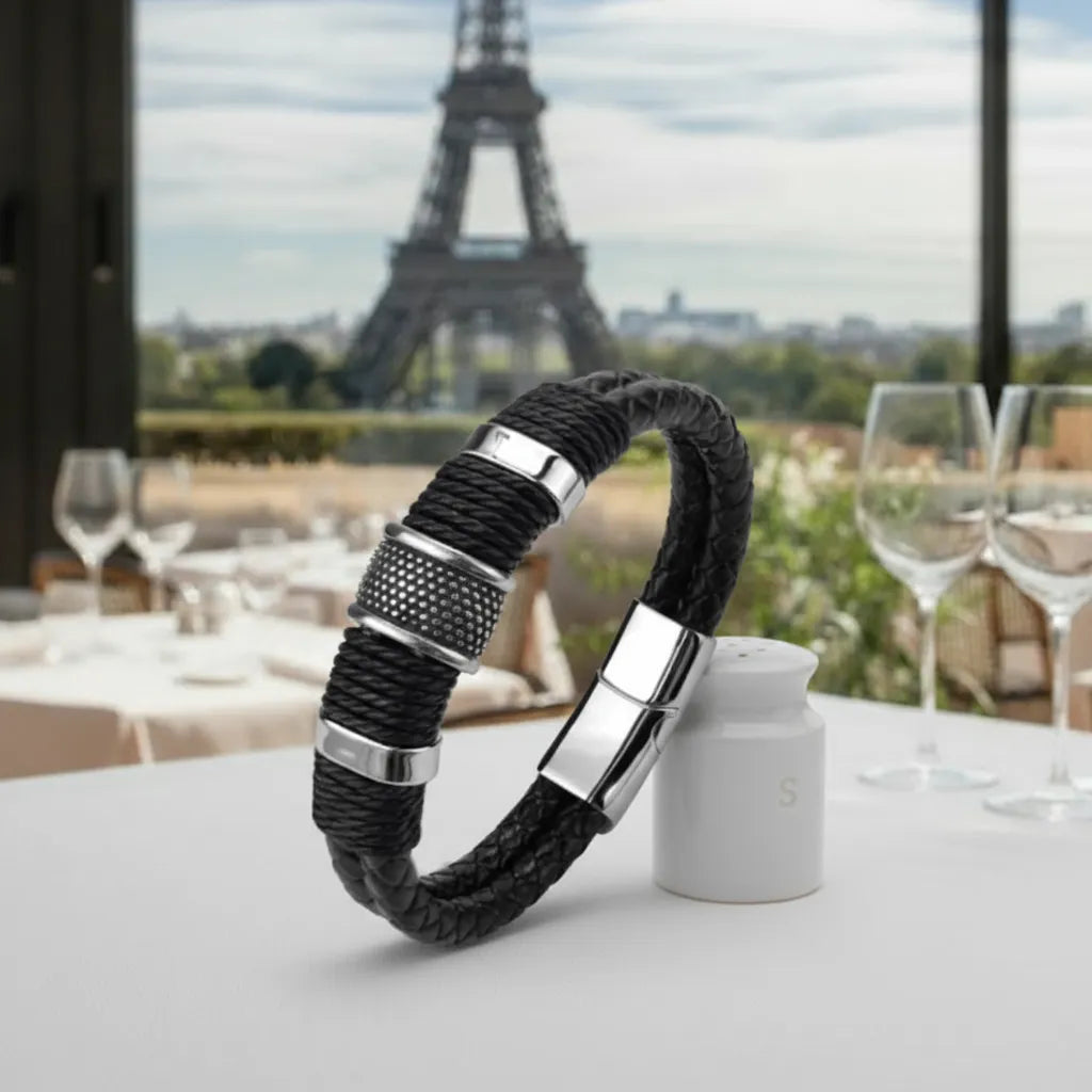 Le bracelet en cuir noir dressé contre une salière. Détail du Cylindre Pointillé capturant la lumière dans l'ambiance structurée du restaurant.