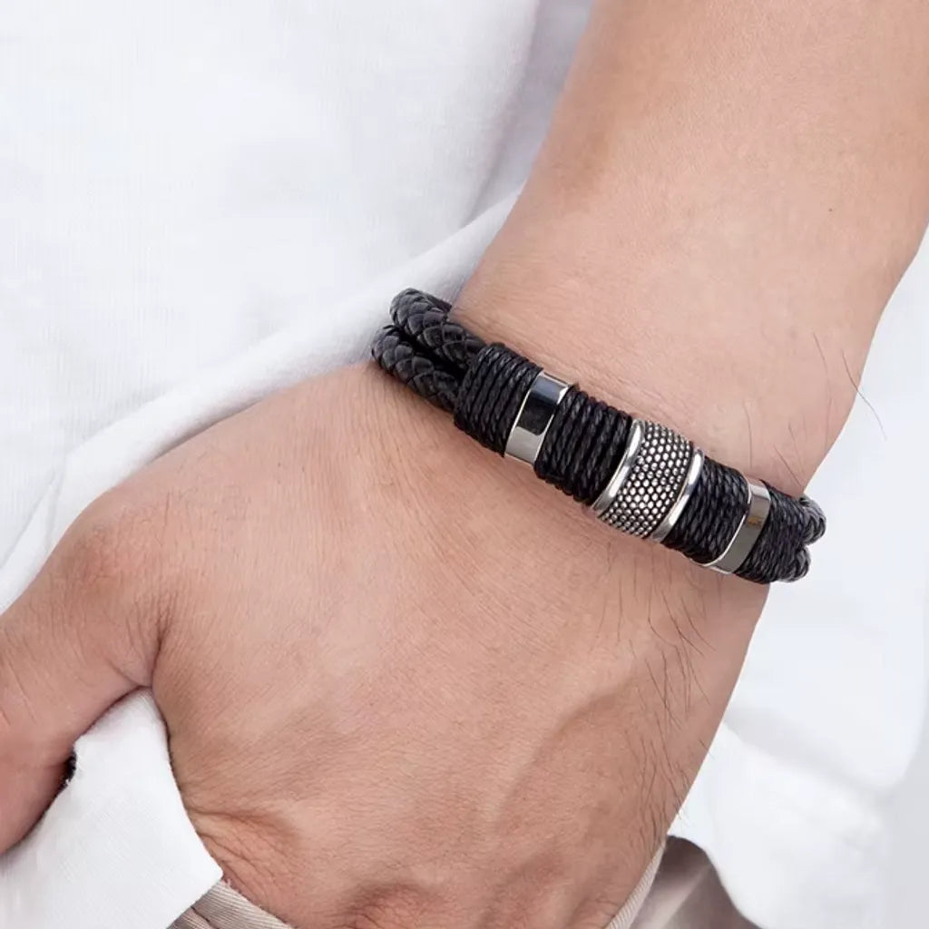 Très gros plan. Le bracelet Cylindre Pointillé en cuir noir au poignet de l'homme. Le cylindre précis contraste avec le t-shirt blanc, la main étant dans la poche.