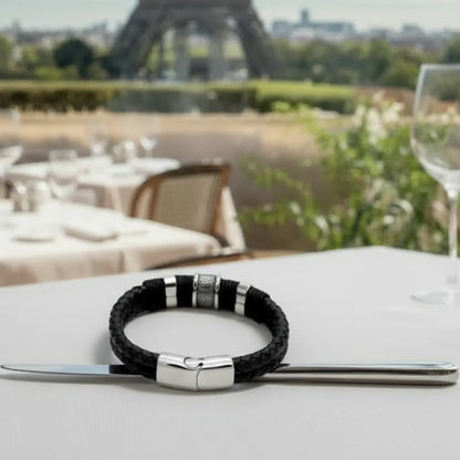 Plan rapproché du bracelet Cylindre Pointillé chevauchant un couteau. Le contraste entre le cuir noir tressé et l'acier inox poli est saisissant.