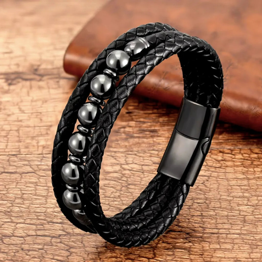 Bracelet en cuir noir tressé orné de perles noires en hématite brillante, posé sur une surface boisée élégante, reflétant une allure moderne et intemporelle.