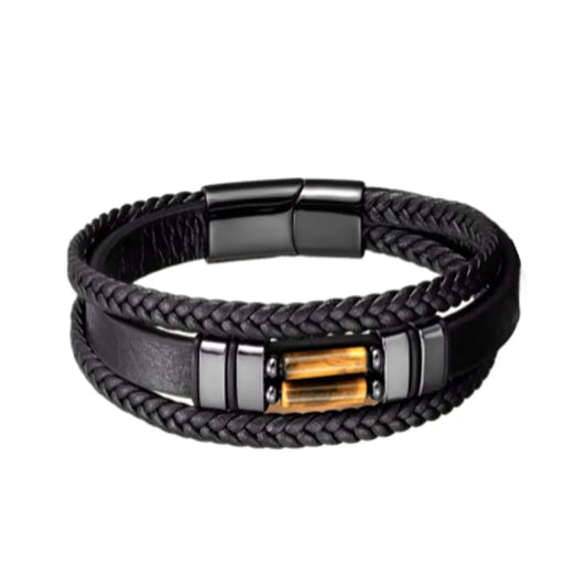 Bracelet en cuir noir tressé avec un design audacieux, sublimé par des perles œil de tigre jaune doré. Le contraste des matériaux et des couleurs est magnifiquement mis en lumière sur un fond uni.