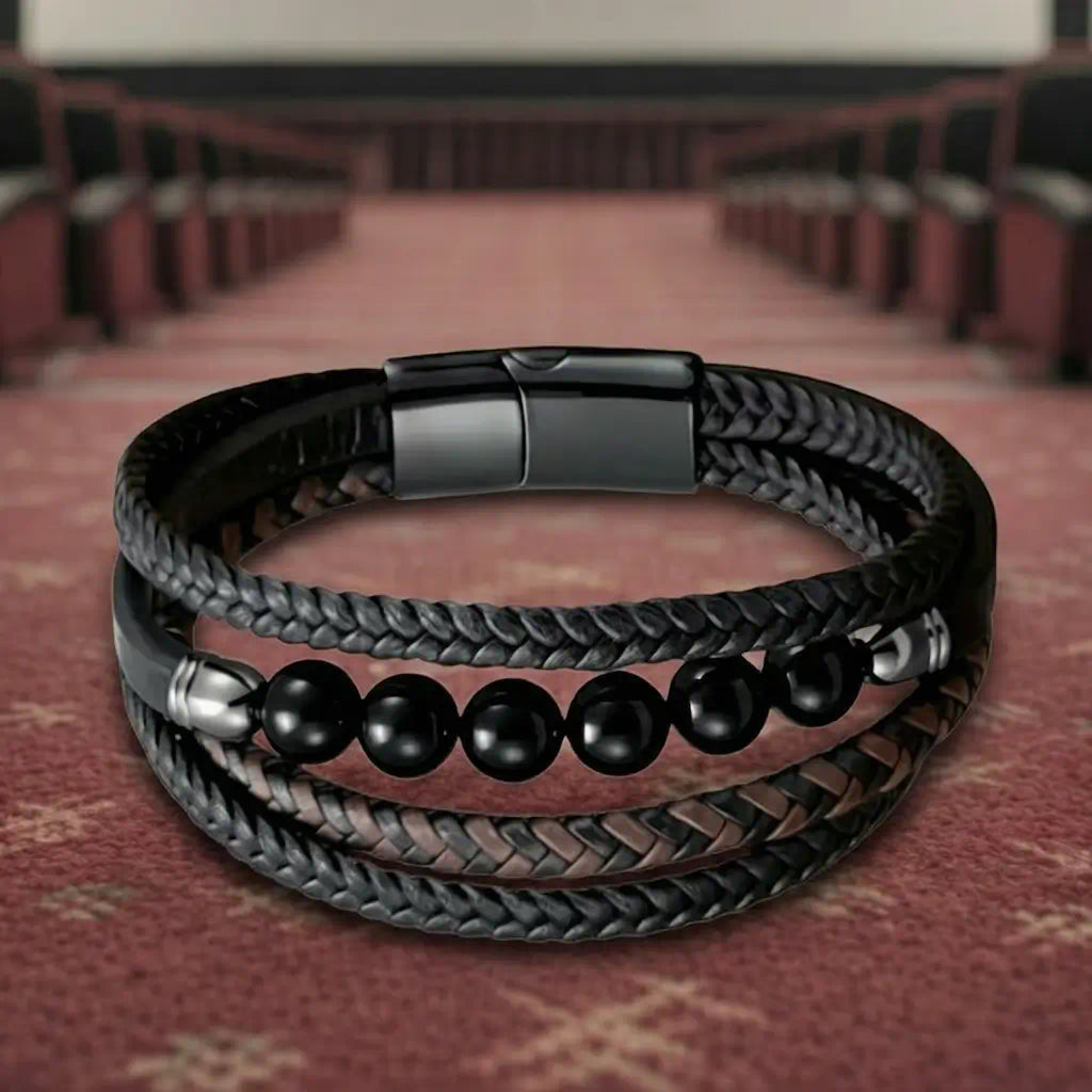 Le bracelet Oris posé à plat sur le sol d'une salle obscure, soulignant la souplesse de ses lanières de cuir. Le motif central d'agate noire et le fermoir magnétique ressortent face à la clarté lointaine de l'image.