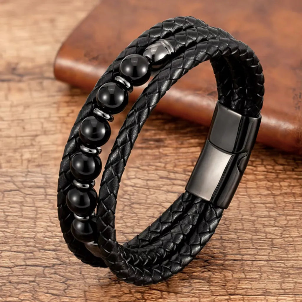 Bracelet en cuir tressé noir avec des perles en agate noire, présenté sur un arrière-plan en bois texturé, idéal pour un style sobre et élégant.