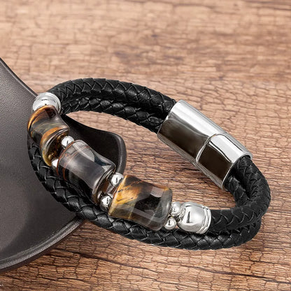 Bracelet en cuir noir tressé, orné de trois pierres œil de tigre jaune, bleu, rouge rectangulaires, présenté sur un fond en bois naturel texturé. Ce bijou élégant associe charme et style moderne, parfait pour un look masculin élégant.