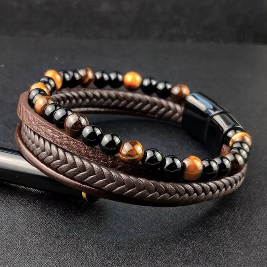 Bracelet élégant pour homme en cuir marron tressé, orné de perles onyx noir brillant et de perles œil de tigre jaune. Le design raffiné est posé sur un fond noir, mettant en valeur les contrastes des matériaux et des couleurs pour un style masculin intemporel.