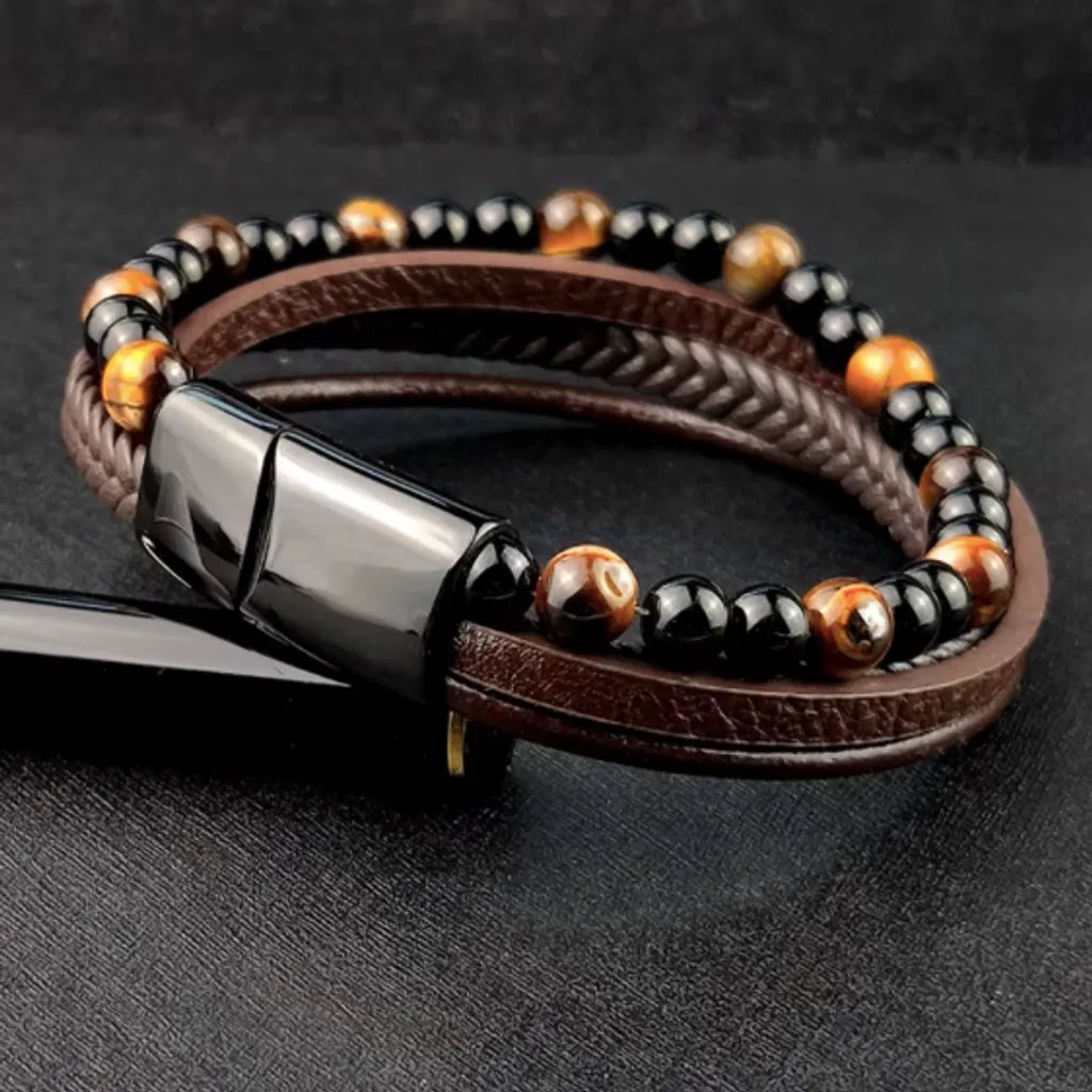 Bracelet en cuir marron et perles de pierres naturelles, vu par l’arrière avec un intérêt sur le fermoir magnétique noir en acier inoxydable brillant. L’accessoire est incliné sur un stylo noir, soulignant son design moderne et fonctionnel, capturé sur un fond sombre.