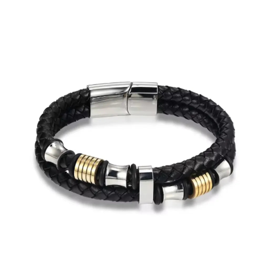 Bracelet en cuir tressé noir orné de perles diabolo argentées et de cylindres dorés. Son fermoir magnétique en acier argenté complète un design moderne et sophistiqué. Présenté sur un fond blanc, ce bracelet met en avant son élégance et la finesse de ses matériaux.