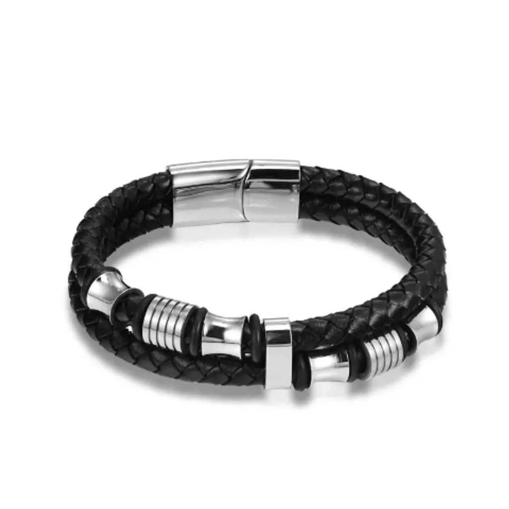 Bracelet en cuir tressé noir équipé de perles diabolo et de cylindres en acier argenté, y compris le fermoir magnétique. Ce design monochrome et épuré, capturé sur un fond blanc neutre, met en valeur la brillance et l'élégance intemporelle de l'acier argenté.