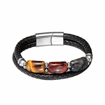Bracelet en cuir noir tressé décoré de trois pierres œil de tigre colorées : une jaune, une rouge et une bleue. Les contrastes vibrants des pierres avec l’acier poli créent un bijou remarquable.
