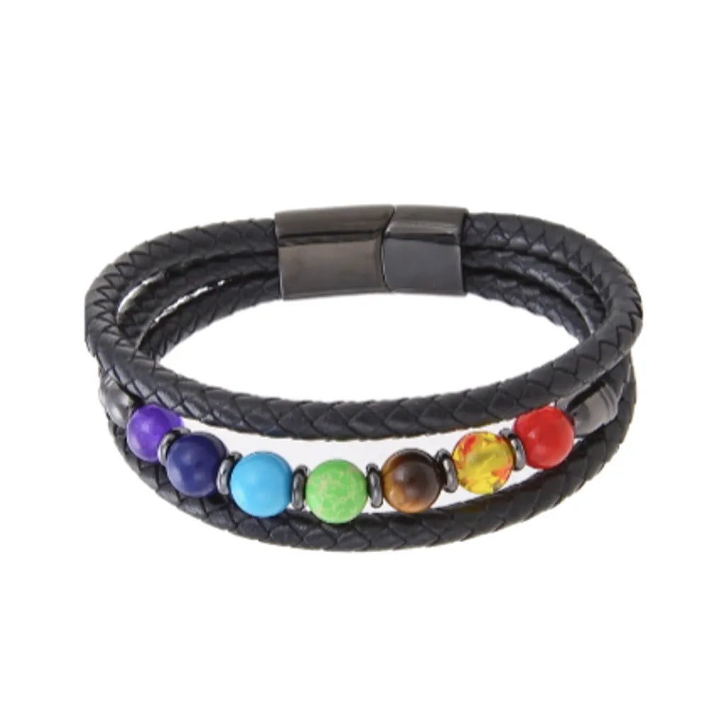 Bracelet en cuir tressé noir avec sept perles représentant les chakras, chacune de couleur vive, alignées au centre et séparées par des anneaux métallique noir. Le bijou est complété par un fermoir magnétique, noir, robuste et élégant, offrant un design équilibré et spirituel.