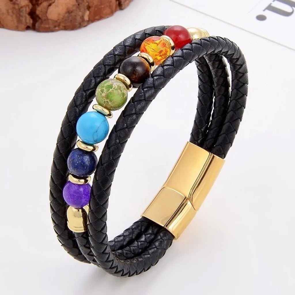 Bracelet élégant en cuir noir tressé avec sept pierres naturelles aux couleurs des chakras. Les anneaux d'espacement dorés et le fermoir magnétique doré apportent une touche sophistiquée, rehaussant le caractère spirituel de ce bijou. L’arrière-plan blanc lumineux souligne les finitions haut de gamme.