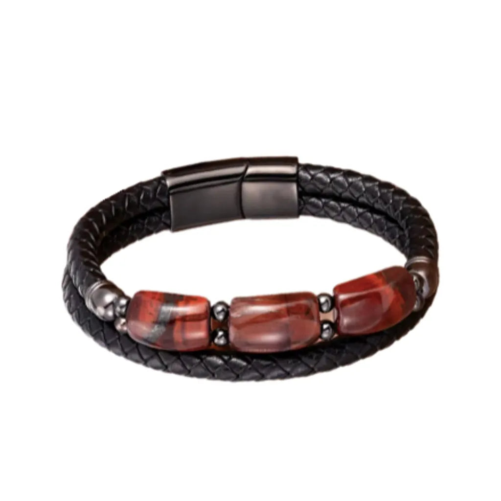 Bracelet en cuir noir tressé, orné de trois pierres œil de tigre rouge intense, entourées d’accents en acier noir. Une pièce unique qui combine style moderne et détails éclatants pour une allure affirmée.