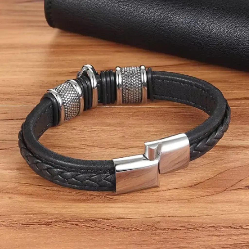 Bracelet en cuir tressé noir, vu de l’arrière avec le fermoir magnétique légèrement entrouvert, posé à plat sur une table en bois, révélant la qualité de l’attache et le style raffiné.