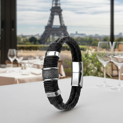 Ce bracelet Cylindre Pointillé en cuir noir est posé avec précision sur la table, reflétant l'architecture de la tour Eiffel vue depuis le restaurant.