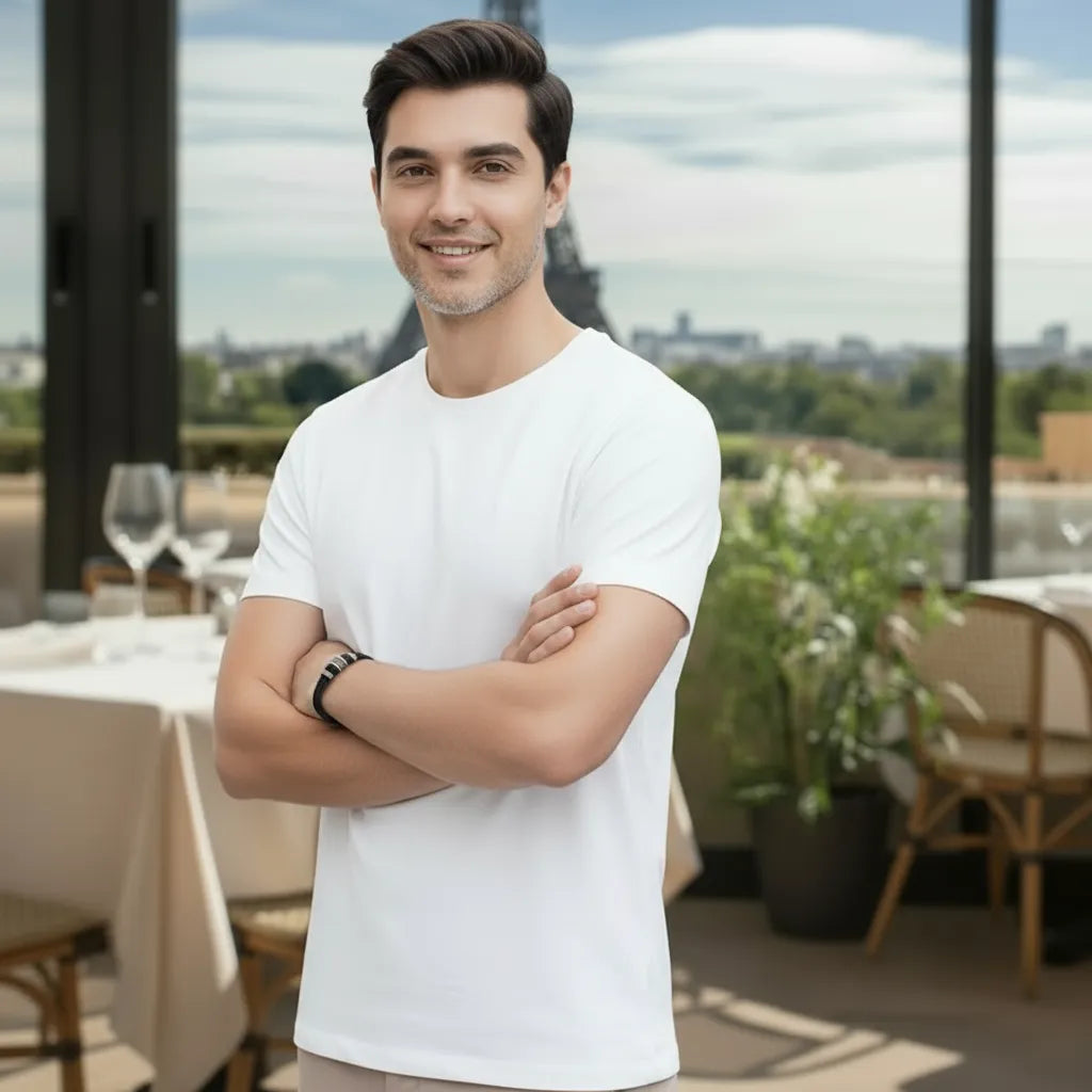 Plan poitrine. L'homme, bras croisés, le bracelet Cylindre Pointillé Cuir Noir au poignet. Le bijou souligne son assurance devant la vue de la tour Eiffel.