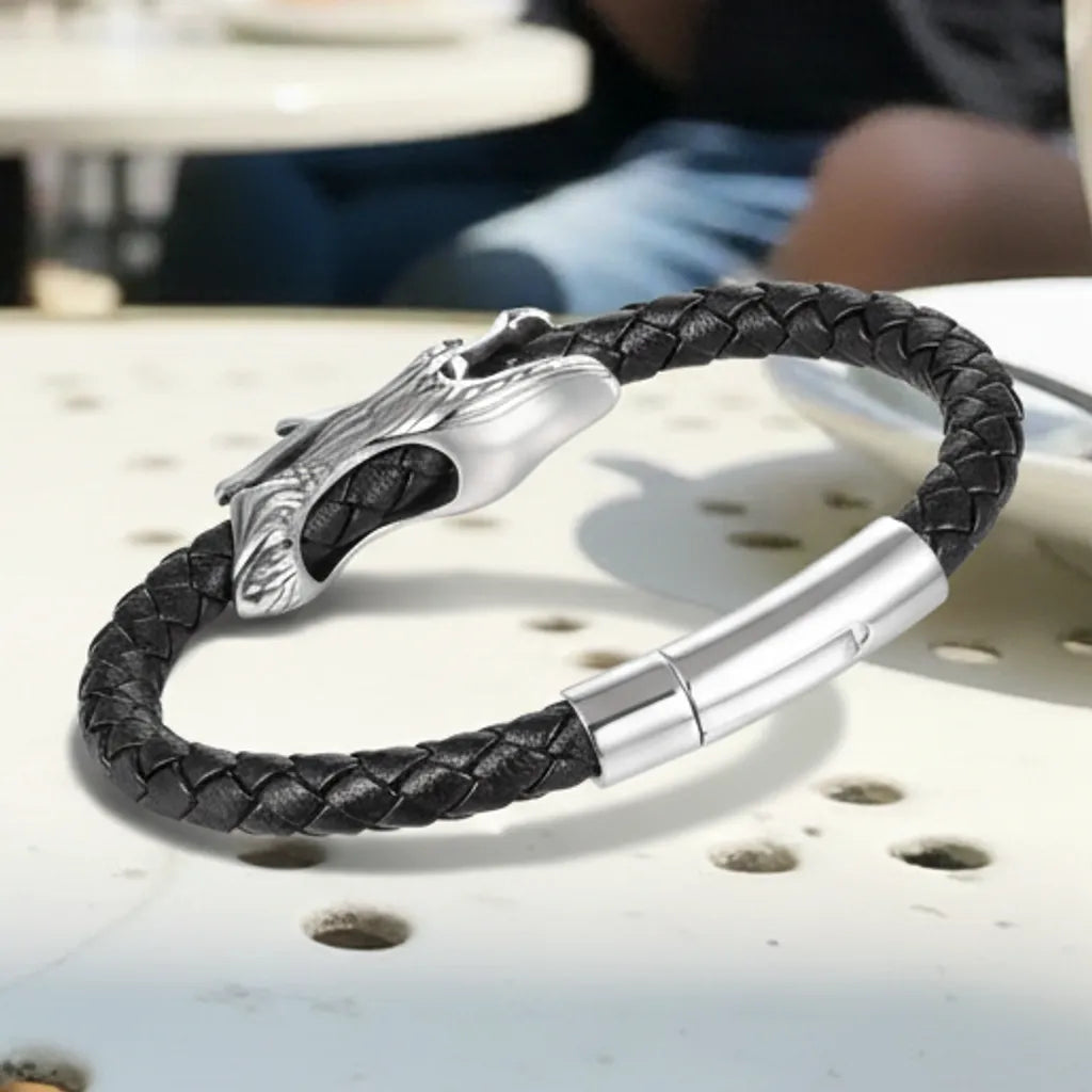 Gros plan du bracelet. Le cuir tressé noir et le fermoir magnétique sont vus de face. On distingue l'arrière lisse du dragon.
