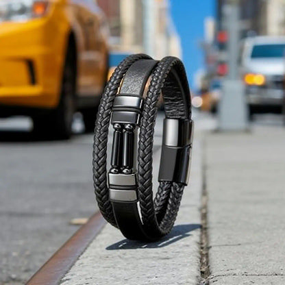 Le bracelet Éclipse se dresse avec autorité sur un bitume urbain, capturant la lumière des gratte-ciel sur ses agates cylindriques et révélant la structure complexe de ses lanières tressées en 3/4 profil.