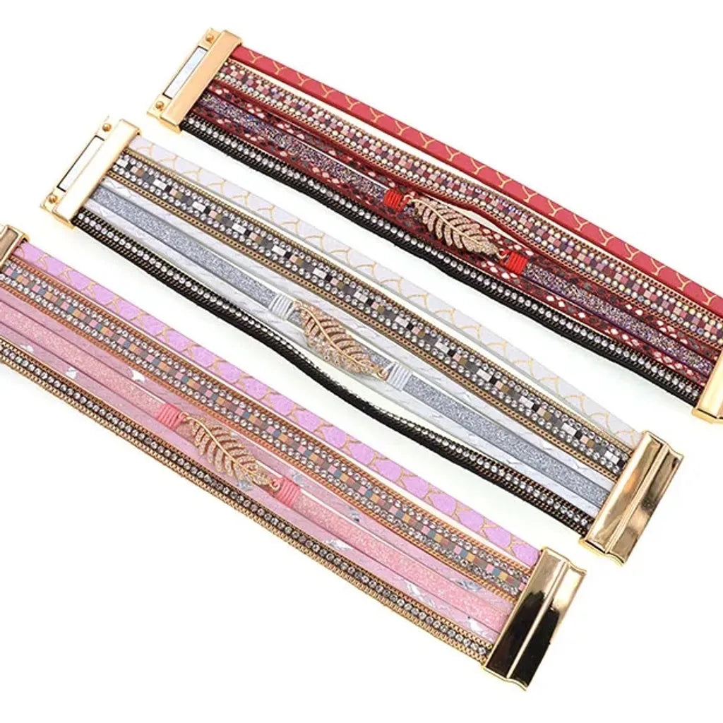 Trio de bracelets Fougère multi-rangs présentés à plat, variations colorées et textures imprimées, finitions dorées et strass.