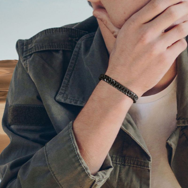 Bracelet gourmette à maillons cubains de douze millimètres avec fermoir sécurisé en acier inoxydable de couleur noir porté par un jeune homme pensif