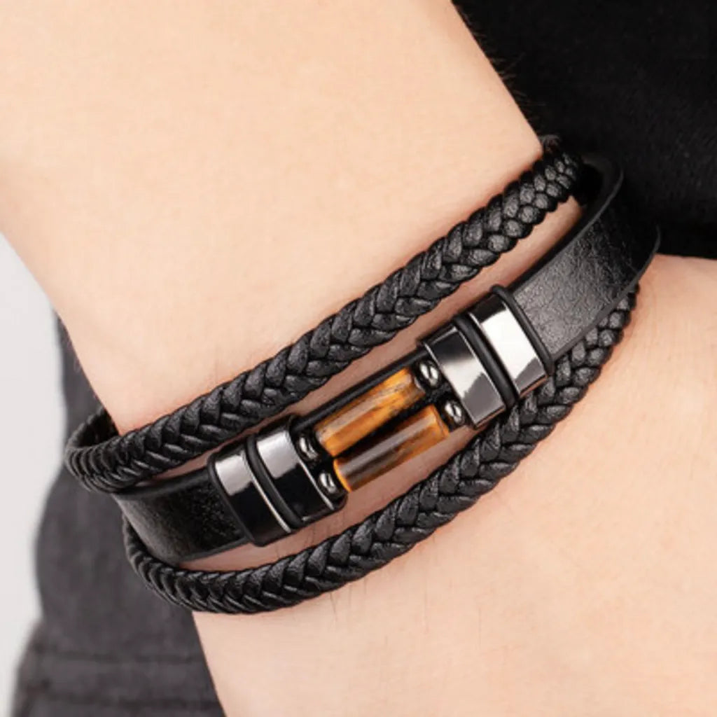 Bracelet en cuir tressé noir avec pierre œil de tigre jaune, porté au poignet droit. Ce bijou masculin allie style moderne et élégance, parfait pour compléter une tenue casual ou formelle.