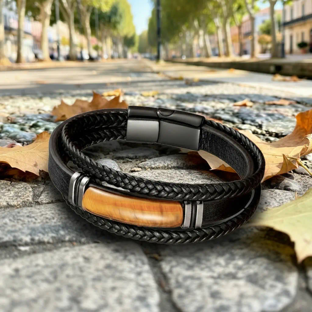 Vue frontale du bracelet multi-rangs reposant sur la pierre brute du chemin, soulignant le contraste entre le cuir noir souple et les quatre bagues d'acier encadrant la gemme brune.