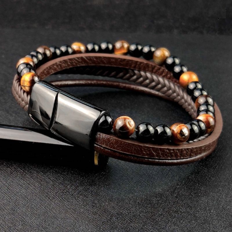 Bracelet de pierres naturelles agate noire et œil de tigre jaune pour homme, son fermoir magnétique en acier inoxydable est noir – posé et incliné sur le capuchon d'un joli stylo   noir avec un liseré doré  – wrap cuir coloris marron.