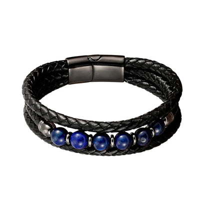 Gros plan du bracelet Azur révélant la texture du cuir noir tressé et l'éclat bleu outremer de six perles naturelles de lapis-lazuli. Le fermoir magnétique en acier gunmetal est visible en arrière-plan sur un décor blanc épuré.